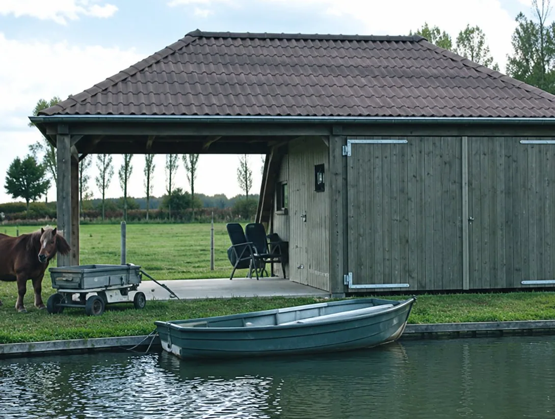 Un abri en bois au toit sombre est construit au bord d'un canal, avec une barque amarrée devant et de l'herbe autour.