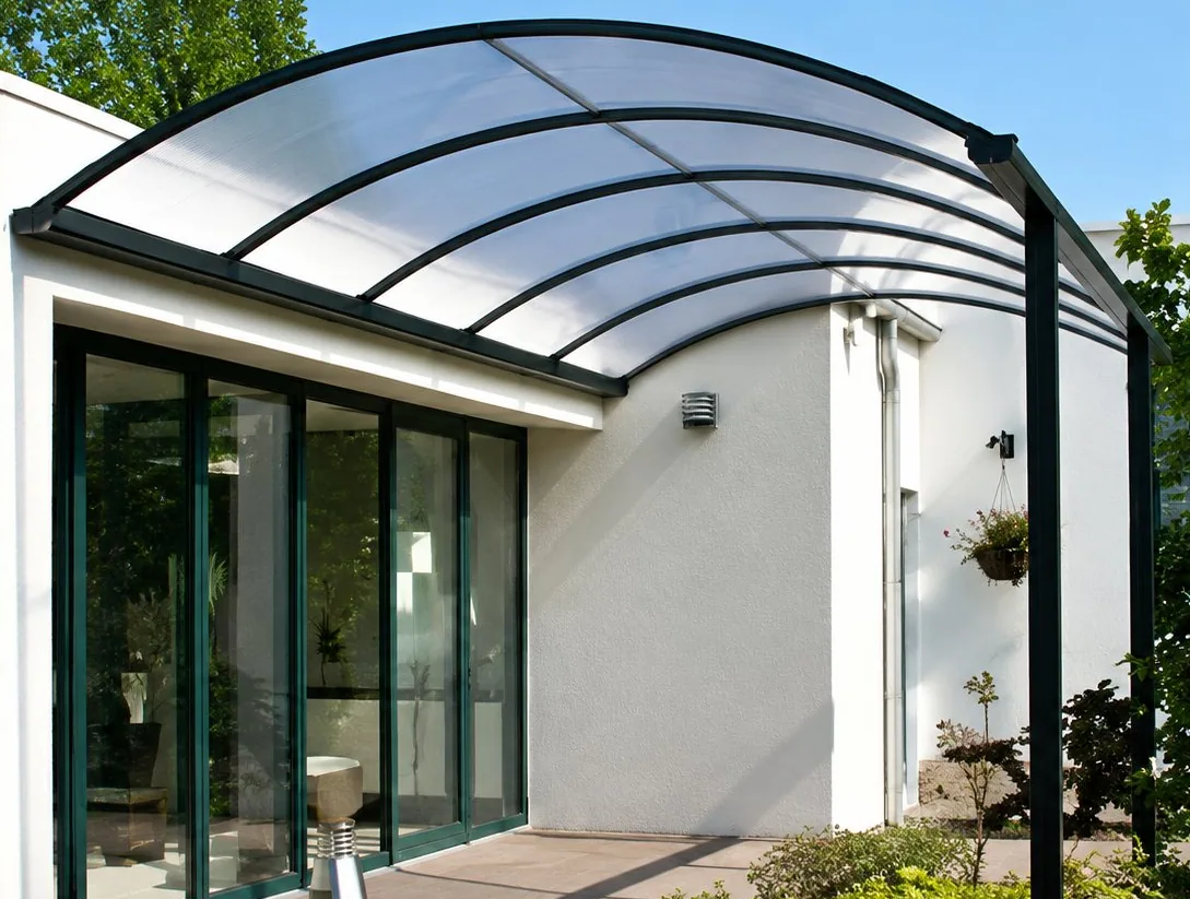 Un auvent arrondi à toit translucide et structure sombre abrite une terrasse devant une maison blanche à grandes baies vitrées.