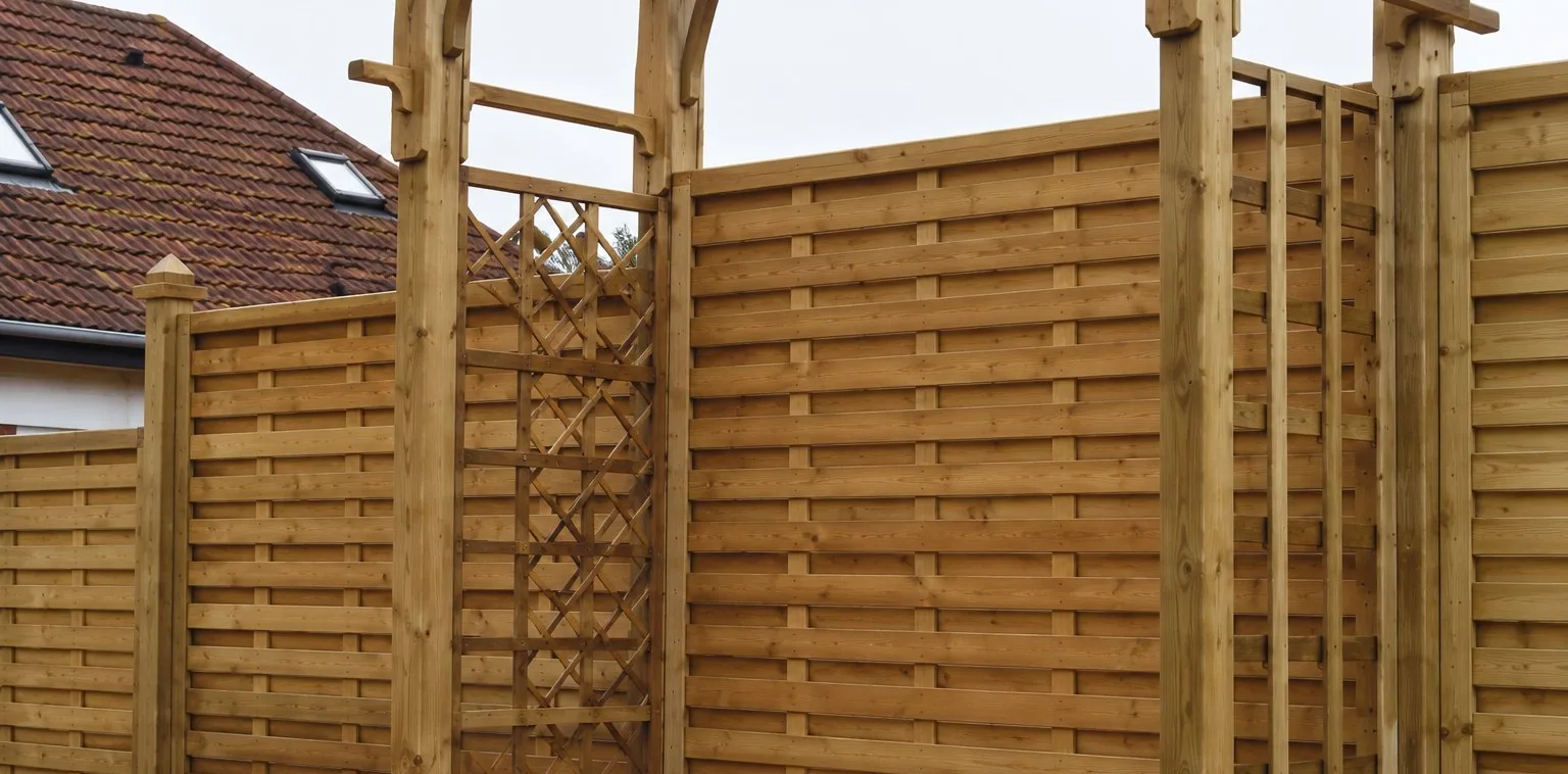 Des panneaux de claustra en bois clair avec lattes verticales et partie ajourée sont installés à l'extérieur, devant une maison.