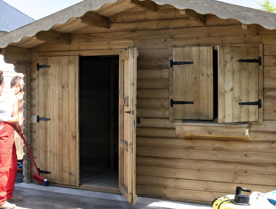 Un petit abri en bois avec des volets et une porte ouverte, photographié en extérieur sous un ciel clair.