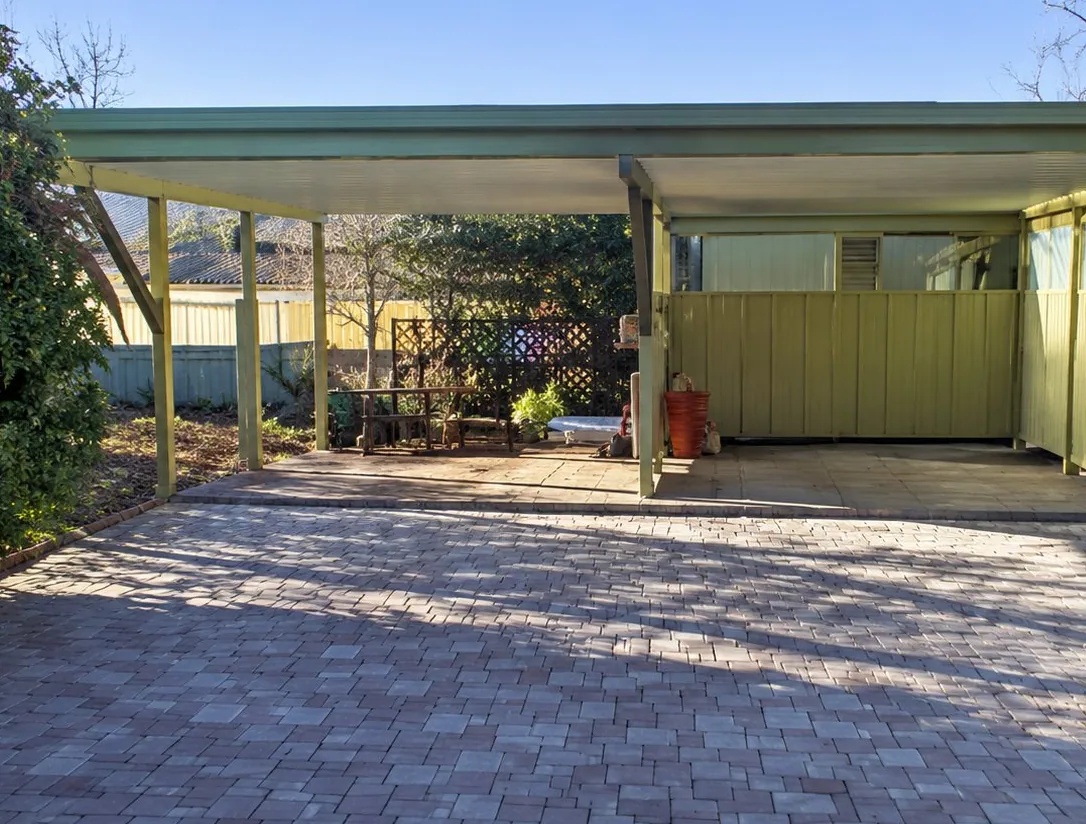 Carport double à toit plat et poteaux verts, devant une grande surface en pavés